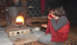 طفلة سورية مع عائلتها تحاول اكتساب الدفء داخل خيمة النزوح بواسطة مدفأة
