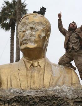 أحد الثوار يعتلي تمثالاً لحافظ الأسد بعد تحرير إدلب