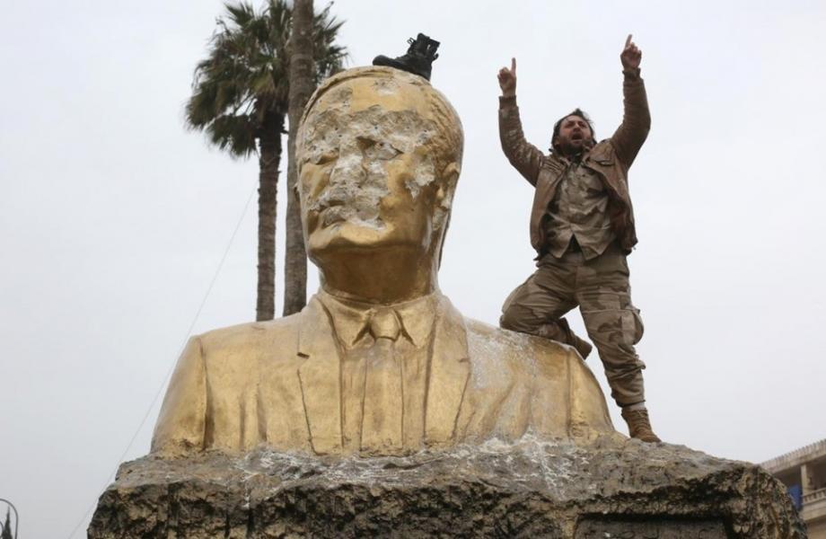 أحد الثوار يعتلي تمثالاً لحافظ الأسد بعد تحرير إدلب